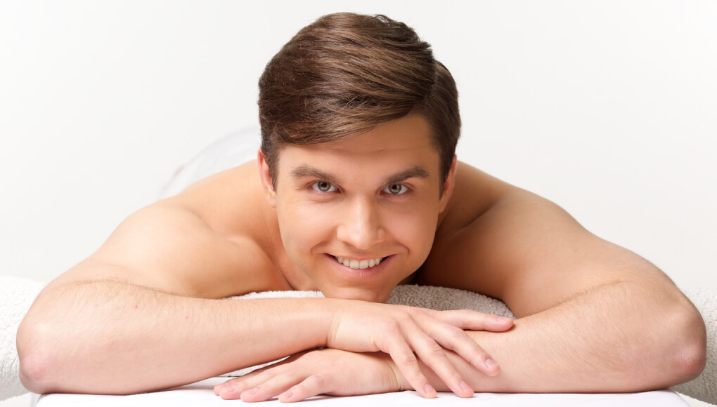 ベッドの上で裸で余裕そうに笑う男性