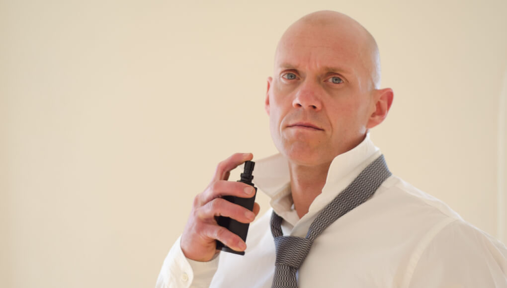 Yシャツをネクタイを付けて香水を振るスキンヘッドの男性